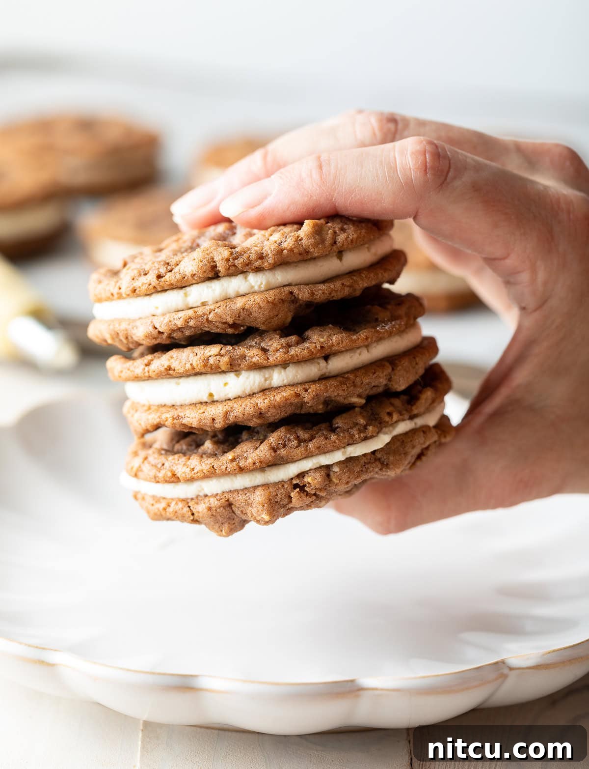 Oatmeal Cream A hand holding three perfectly assembled Homemade Oatmeal Cream Pies above a serving tray.