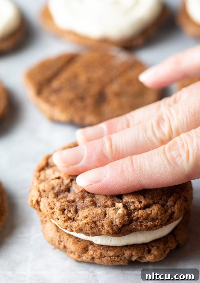 Chewy Oatmeal Cream Pie Bliss 6 A hand gently pressing the top layer of an oatmeal cookie over the cream filling to complete the pie.