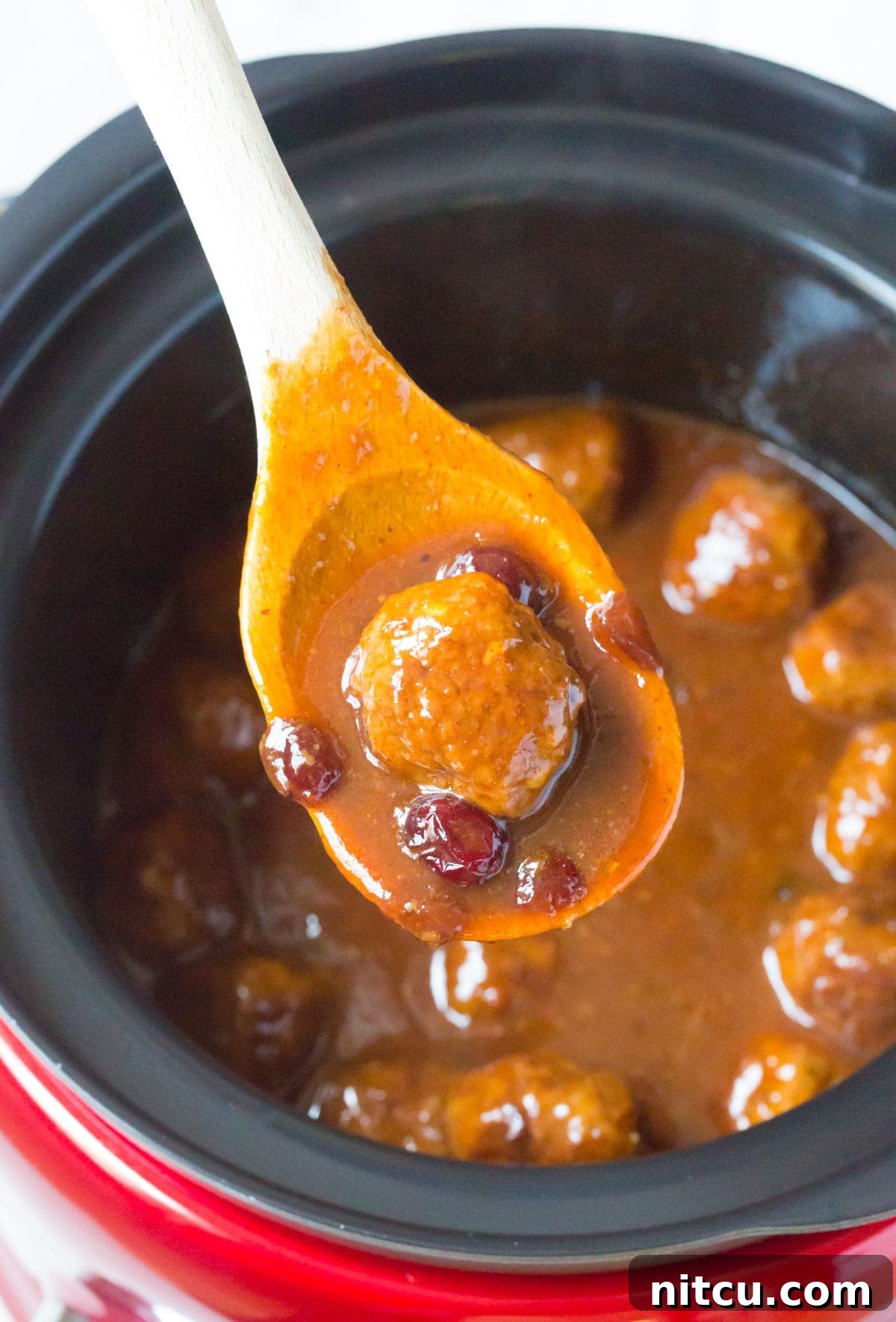 Crockpot Party Meatballs 3 Close-up of a single cocktail meatball on a wooden spoon, coated in rich cranberry BBQ sauce