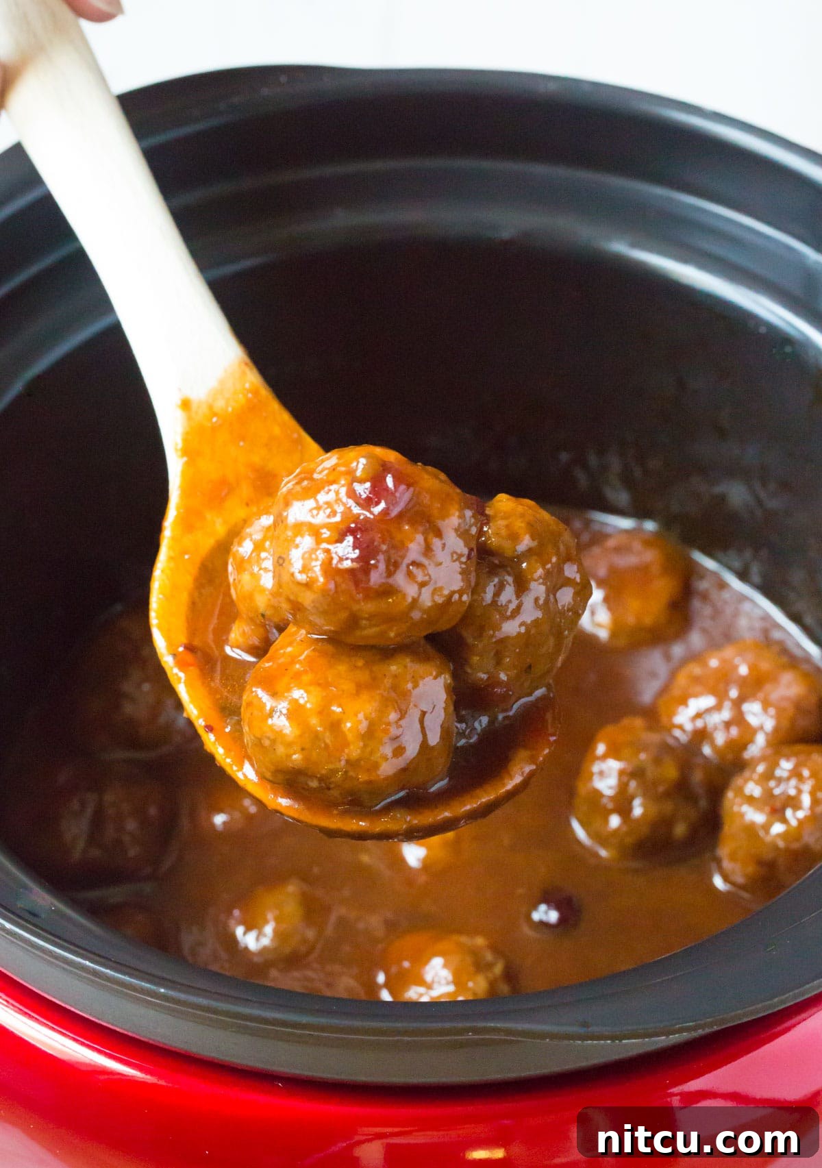 Crockpot Party Meatballs 10 Final presentation of slow cooker cocktail meatballs in sauce on a wooden spoon
