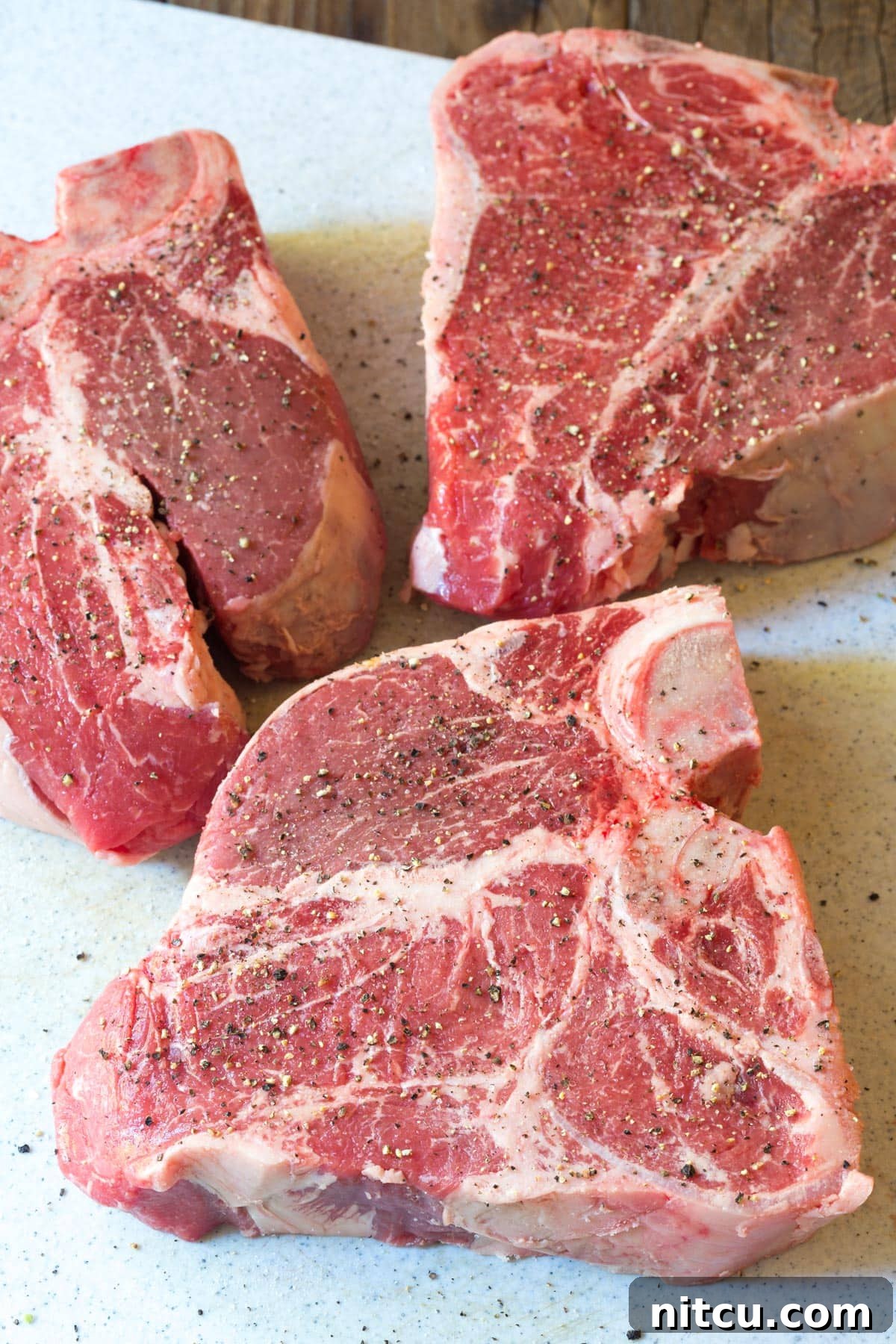 Thick-cut porterhouse steaks for Bistecca alla Fiorentina, seasoned with salt and pepper on a wooden cutting board