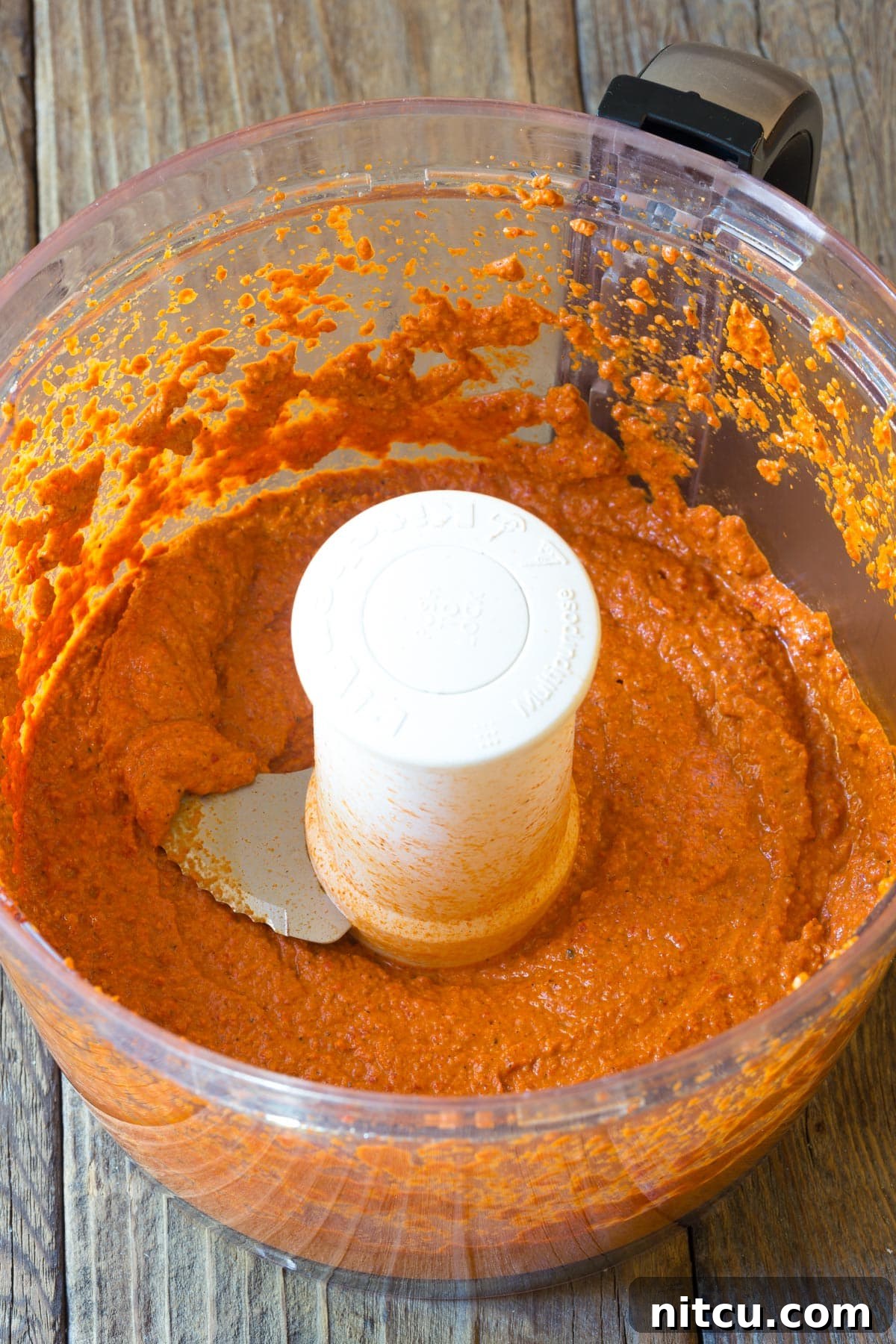 Romesco Sauce being blended in a food processor, showcasing its rich red color and creamy texture