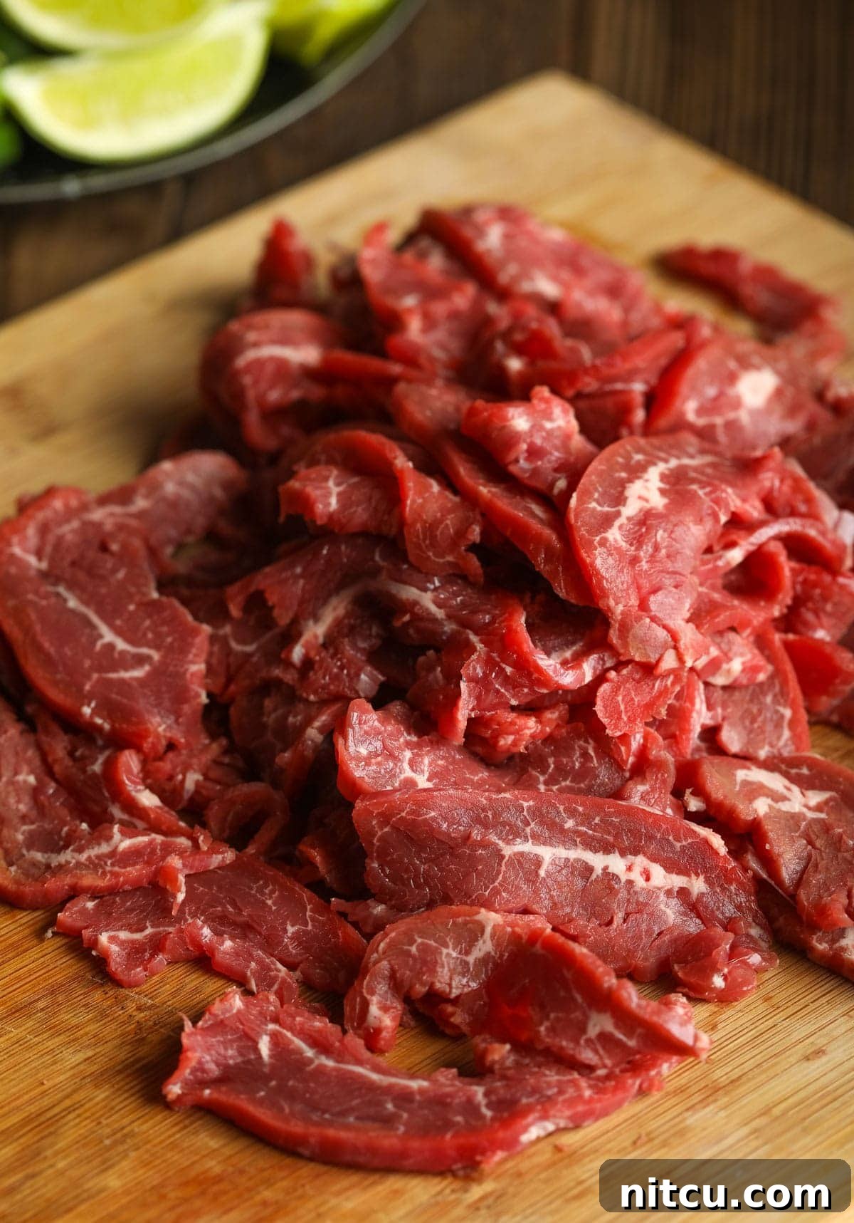 Wholesome Pho Creation 7 Raw flank steak, expertly thinly sliced against the grain on a rustic wooden cutting board, ready for the pho.