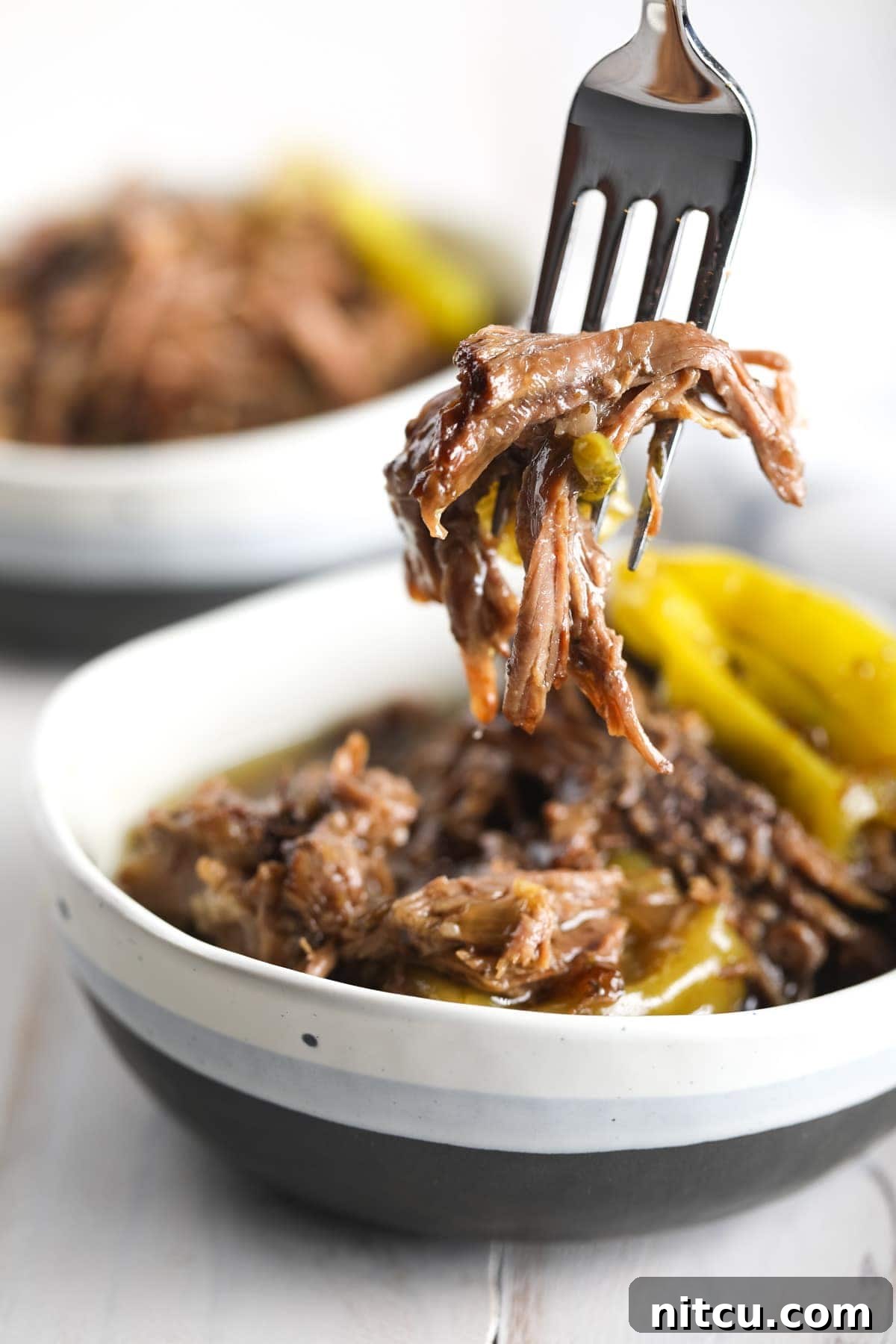 Savory Italian Beef 2 Shredded Instant Pot Italian Beef in a bowl with a fork, garnished with fresh herbs and ready to be served.