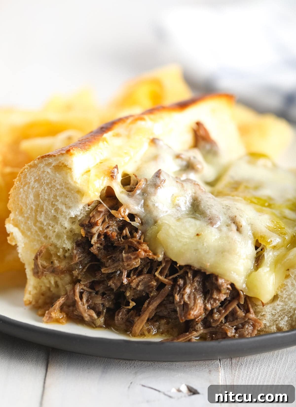 Savory Italian Beef 11 Shredded Instant Pot Italian beef sandwich with perfectly melted provolone cheese on top, served on a white plate with a side of au jus.