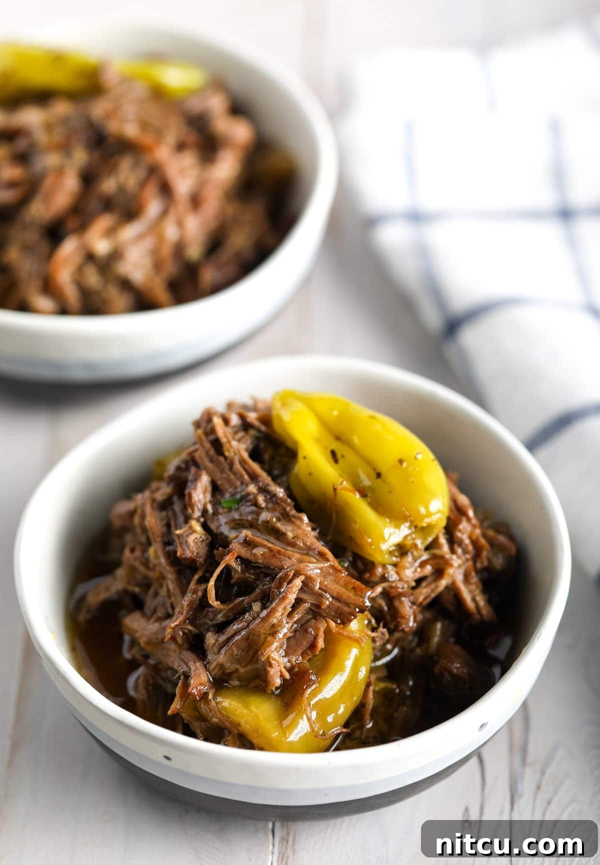Savory Italian Beef 4 Two white bowls brimming with delicious Italian beef and vibrant green pepperoncini peppers, ready to be served.