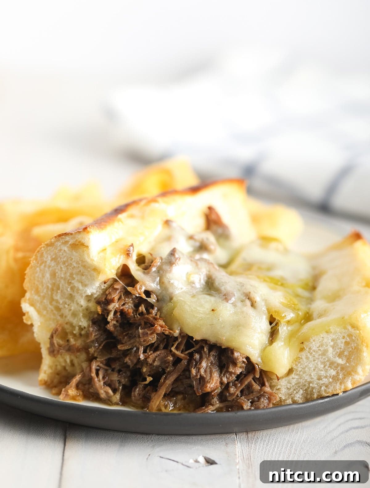 Savory Italian Beef 5 A perfectly prepared Italian beef sandwich with melted provolone cheese, served on a white plate with visible juices.