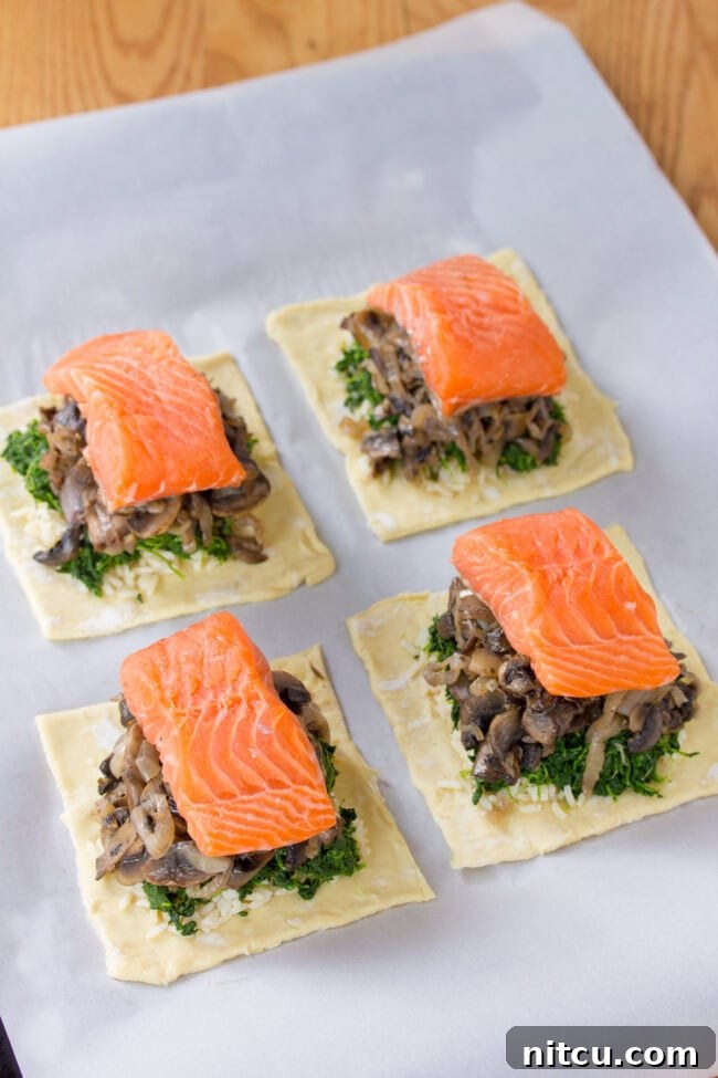 Regal Salmon Pie 7 The process of layering Salmon Coulibiac ingredients: puff pastry, rice, spinach, mushrooms, and salmon fillet arranged meticulously.