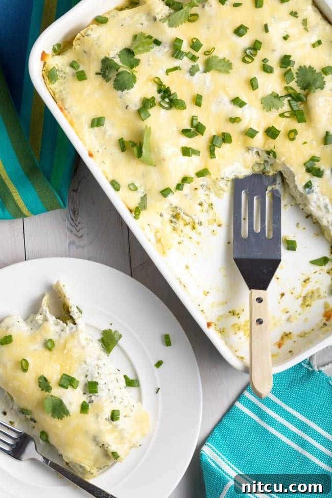Creamy Swiss Enchiladas 4 Enchiladas Suizas in a baking dish with a piece removed, revealing the delicious layers.