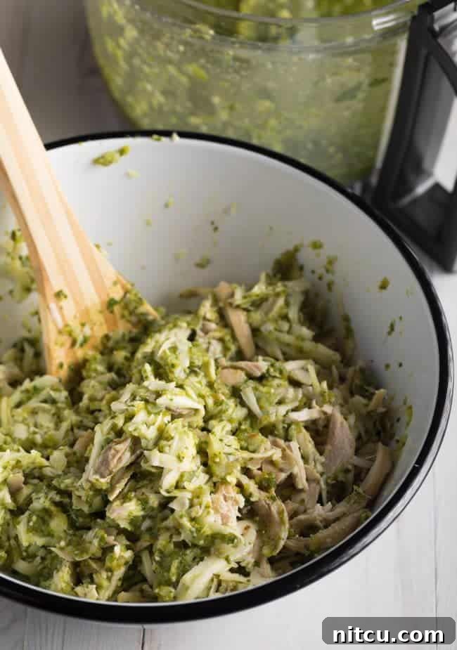 Creamy Swiss Enchiladas 9 Shredded chicken being mixed with salsa verde sauce in a bowl.