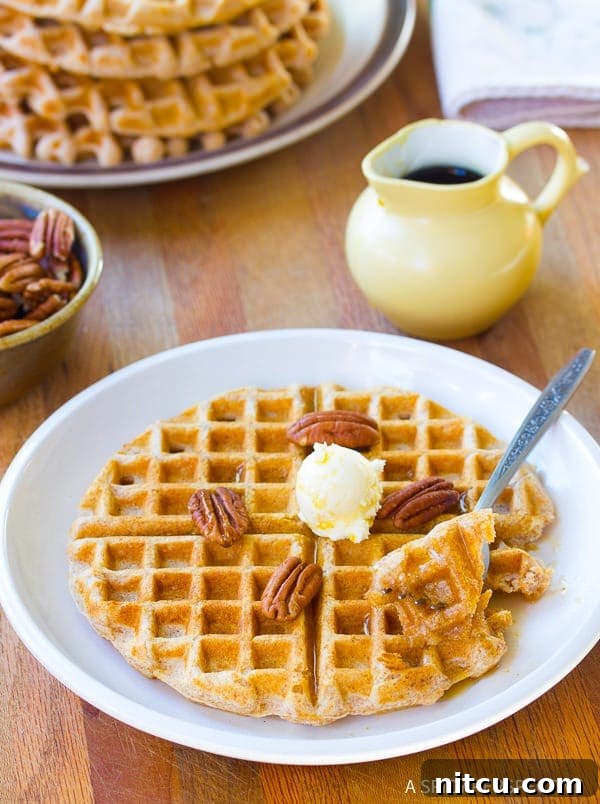 Spelt Flour Waffles stacked high on a plate, garnished with fresh berries and maple syrup.