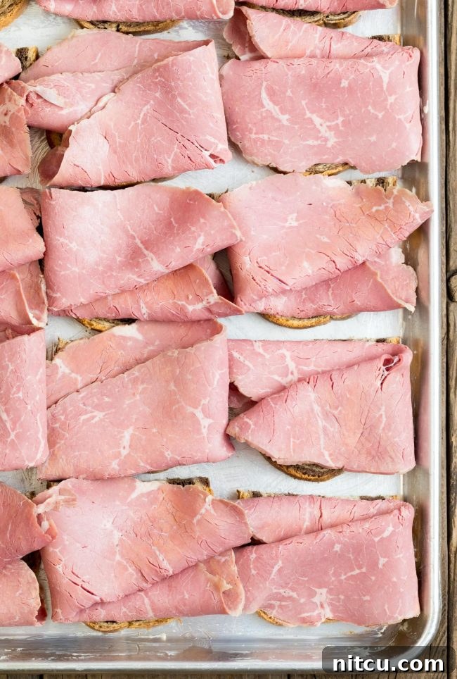 Golden Baked Reuben Sandwich 5 Rye bread assembled with generous slices of corned beef on a sheet pan, ready for the next layer.