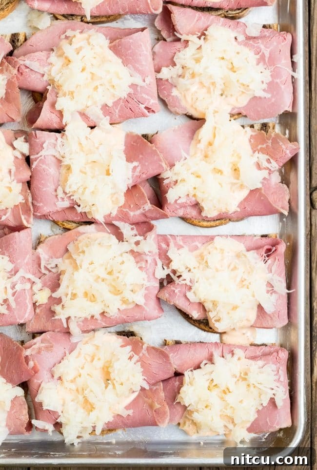 Golden Baked Reuben Sandwich 7 Rye bread topped with neatly arranged corned beef and a mound of sauerkraut on a sheet pan.