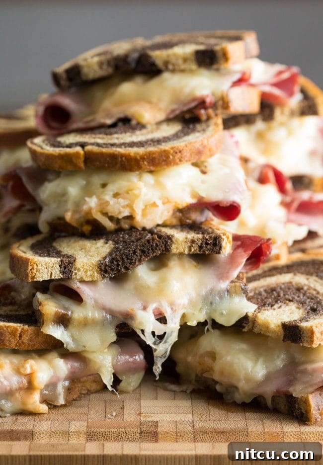Golden Baked Reuben Sandwich 9 Baked Reuben sandwiches generously piled on top of each other, ready to be enjoyed.
