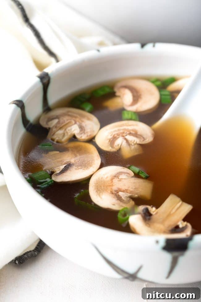 Elegant Dashi Broth 4 Bowl of healthy clear soup with mushrooms and scallions and a large soup spoon.