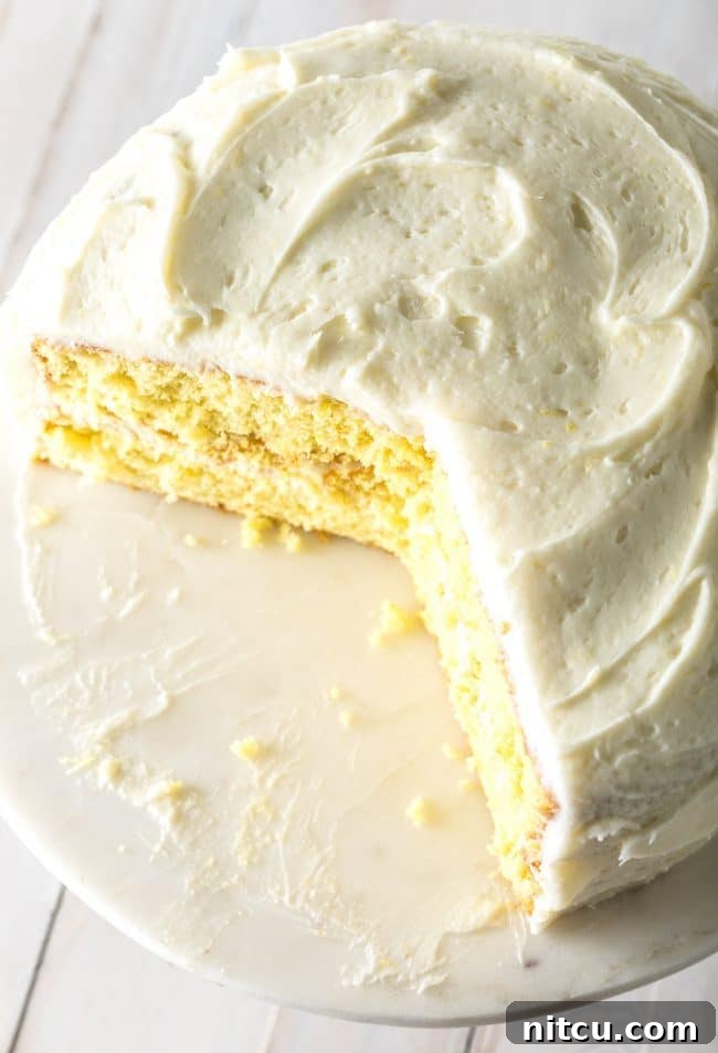 A perfectly cut slice of Lemon Buttermilk Cake with a delicate crumb removed from the main cake, revealing its moist layers and creamy frosting.