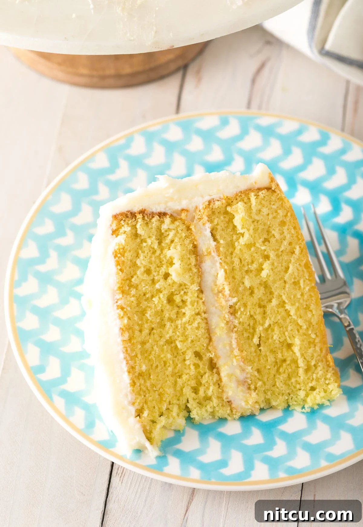 A single, delectable slice of Lemon Buttermilk cake served on a serene blue plate, highlighting its moist crumb and creamy frosting, ready to be enjoyed.