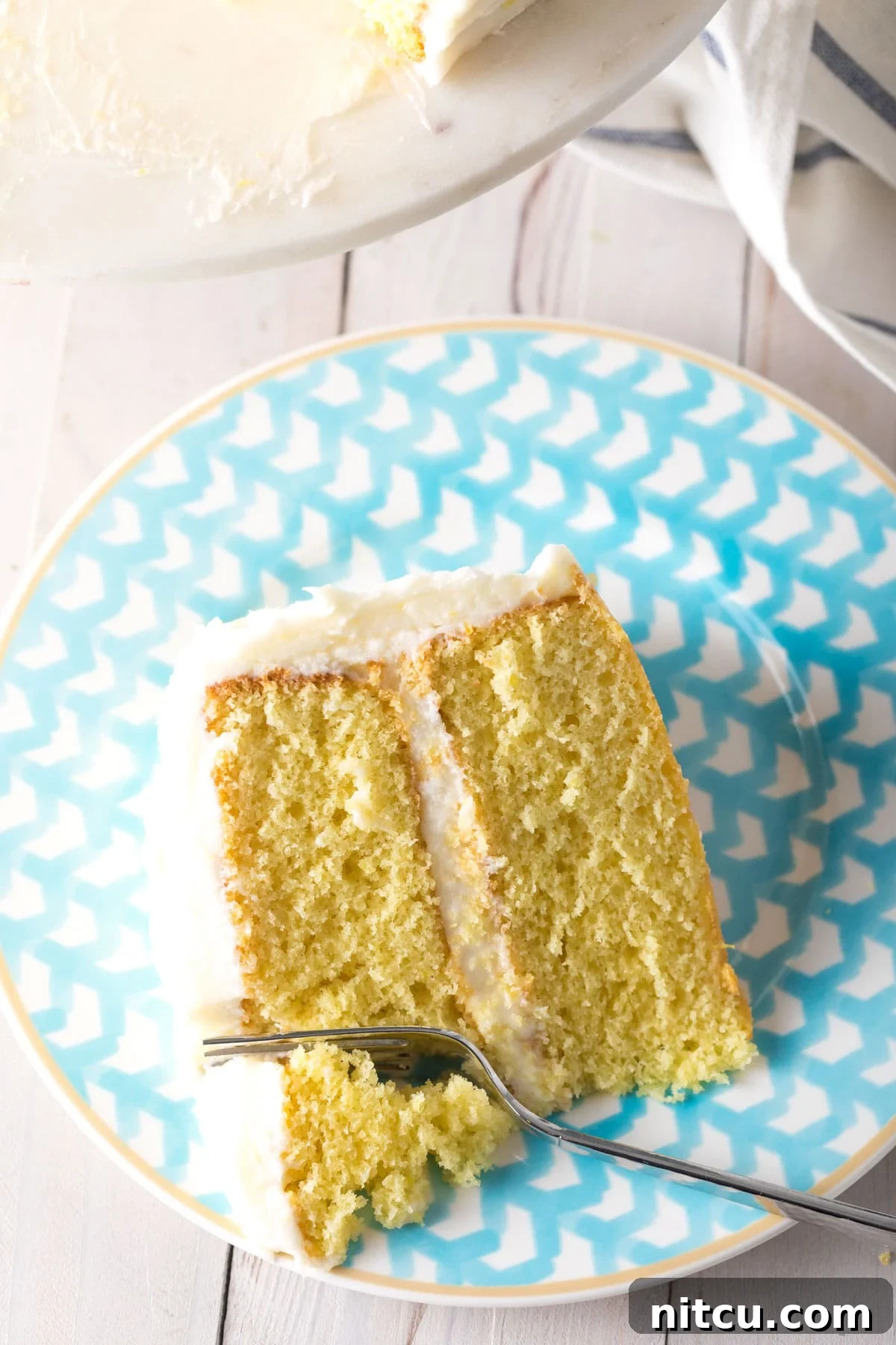 A top-down view of a fork gently taking a bite from a slice of Lemon Buttermilk Cake, highlighting its soft texture and inviting appeal.