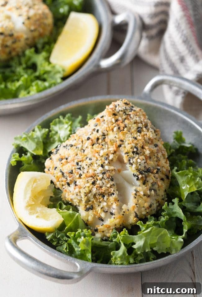Everything Bagel Crusted Cod 2 Baked White Fish with Everything Bagel Crust served on a bed of lettuce with a lemon wedge.