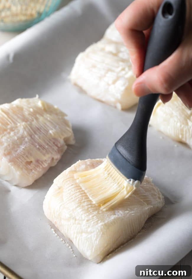 Everything Bagel Crusted Cod 6 Hand using a brush to brush the fish with mayonnaise to help the seasoning bind to the fish.