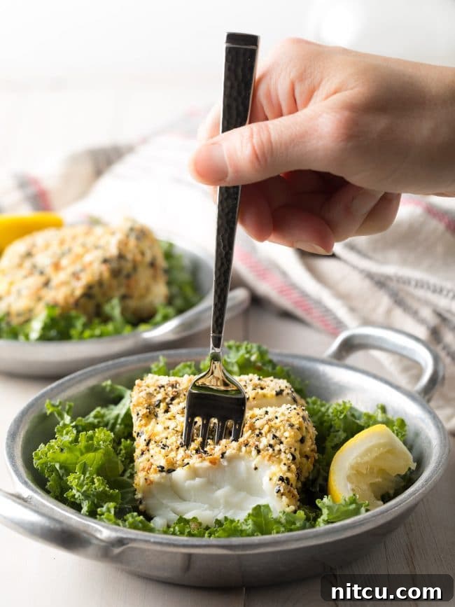 Everything Bagel Crusted Cod 10 Hand using a fork to flake off a piece of fish from the cod.