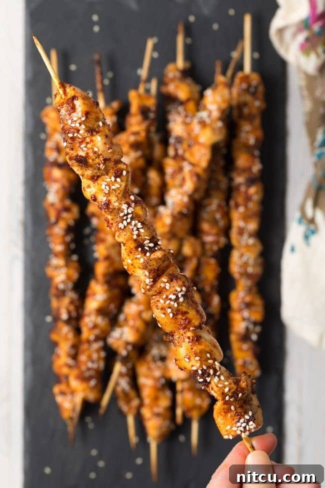 Gochujang Glazed Chicken Skewers 10 Three Korean chicken skewers resting on a wooden board with fresh herbs.