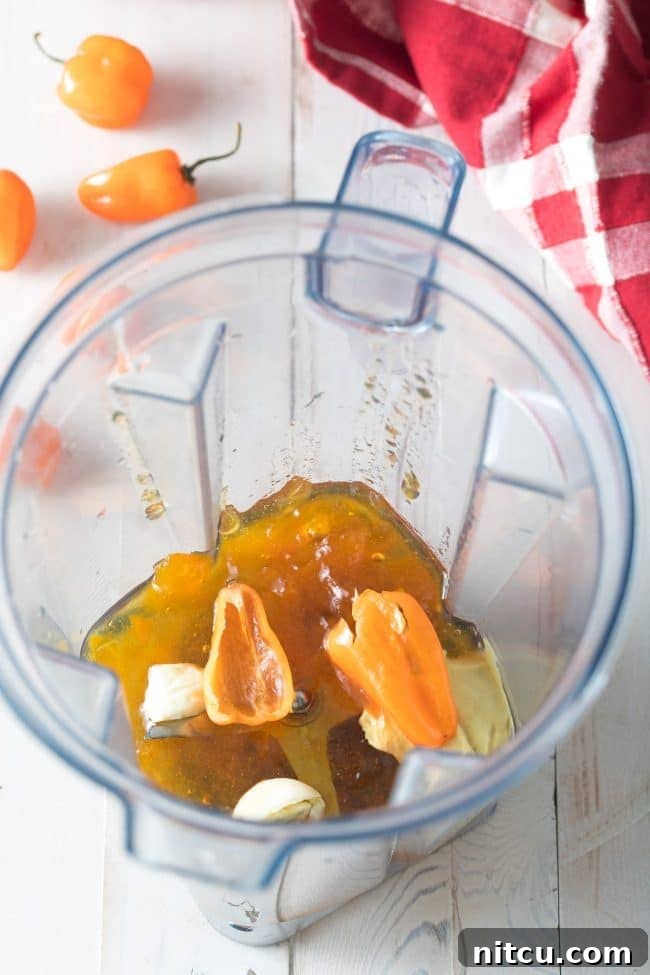 Peach Habanero Flame Wings 4 Halved habanero peppers in a blender jar with peach jam and cloves of garlic.