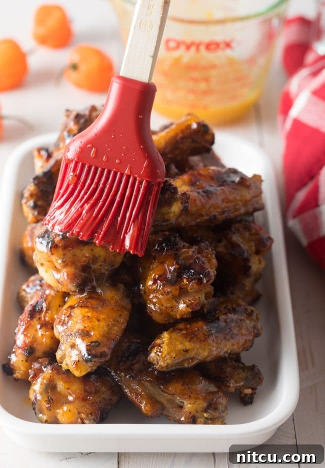 Peach Habanero Flame Wings 6 Using a red pastry brush peach habanero glaze on a plateful of chicken wings.