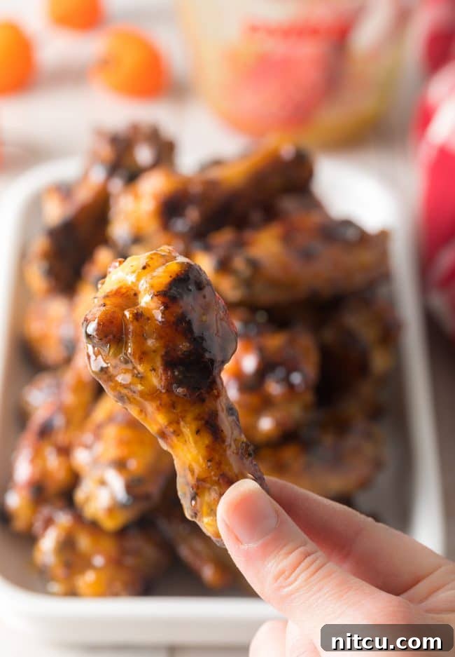 Peach Habanero Flame Wings 8 Hand holding up a drummie glazed wing to camera.