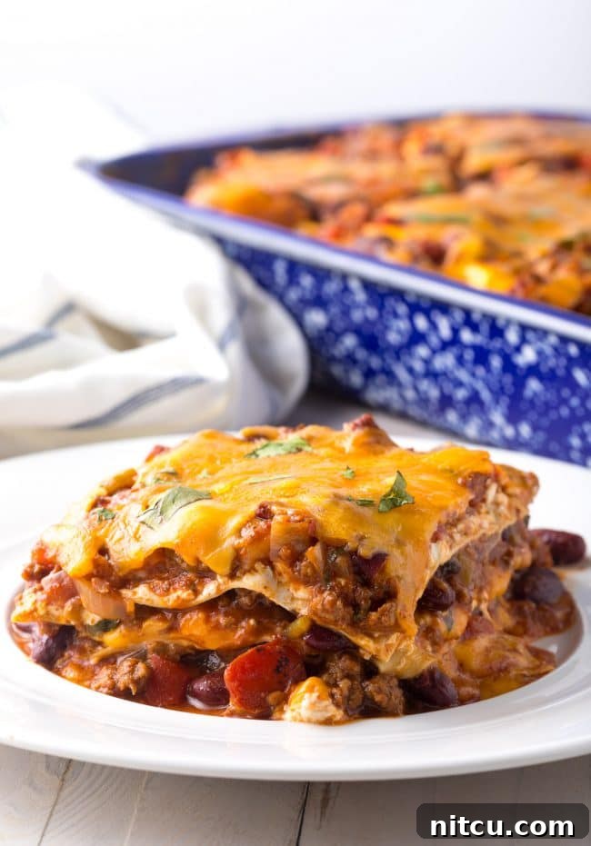 A perfectly portioned slice of Cowboy Chili Lasagna resting on a white plate, showcasing its delicious, multi-layered construction