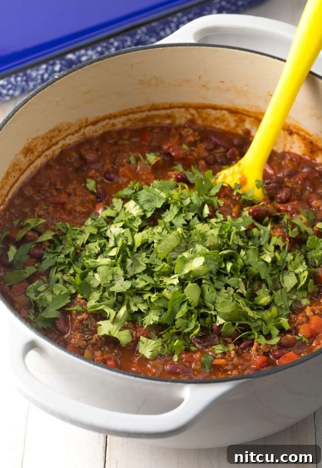 Fresh cilantro being stirred into a pot of freshly cooked Cowboy Chili, adding a burst of freshness