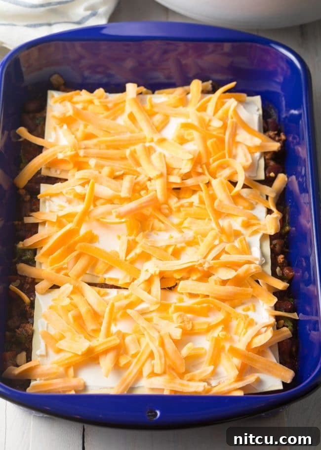 Second layer of Cowboy Chili Lasagna being assembled, with shredded cheese added over the noodles