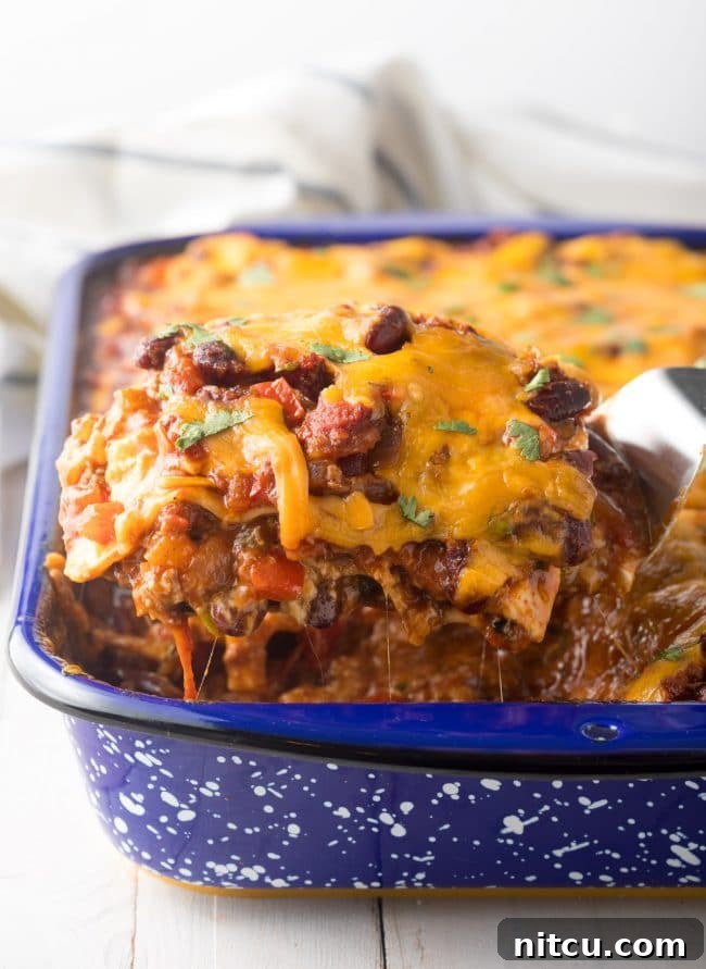 A large, perfectly portioned slice of Easy Chili Lasagna being lifted from the baking pan, clearly showing distinct layers of melted cheese, tender beans, flavorful meat, and rich sauce