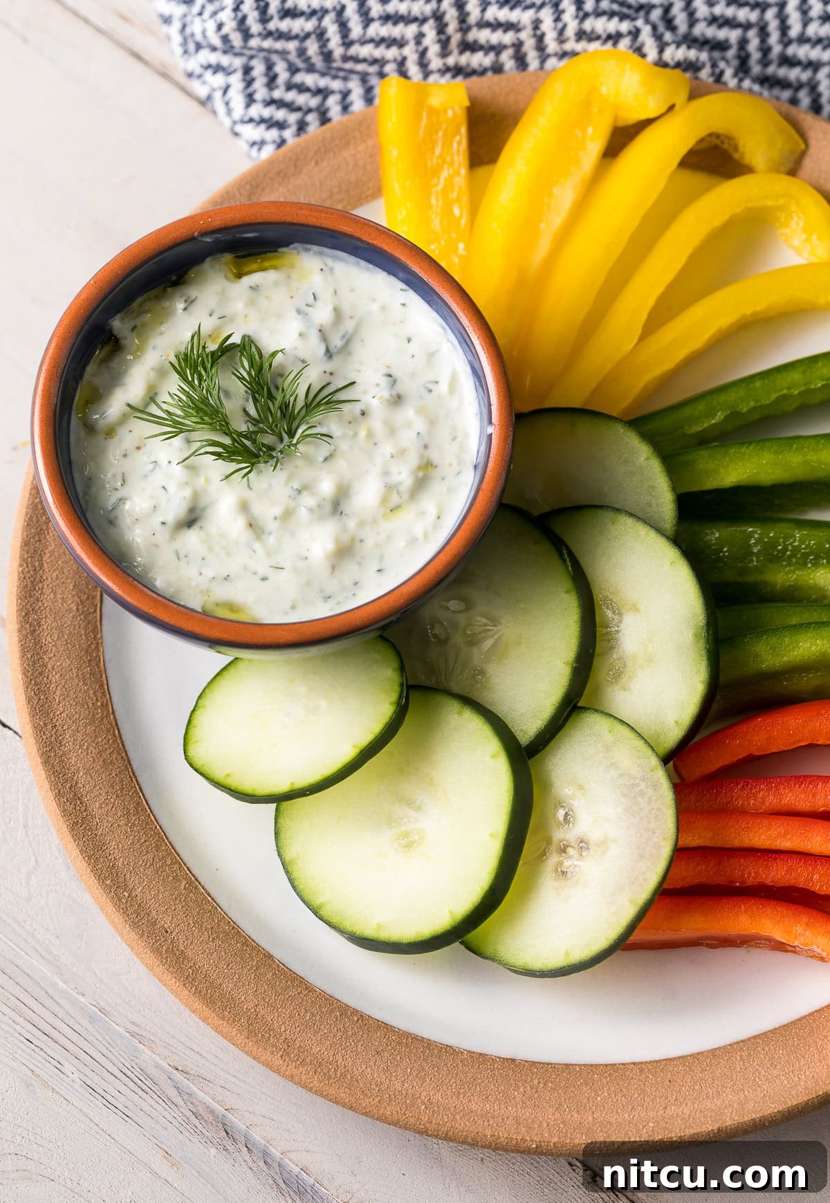 Refreshing Greek Cucumber Dip 4 Tzatziki dip in an orange and blue bowl placed on a serving platter next to cut up veggies.