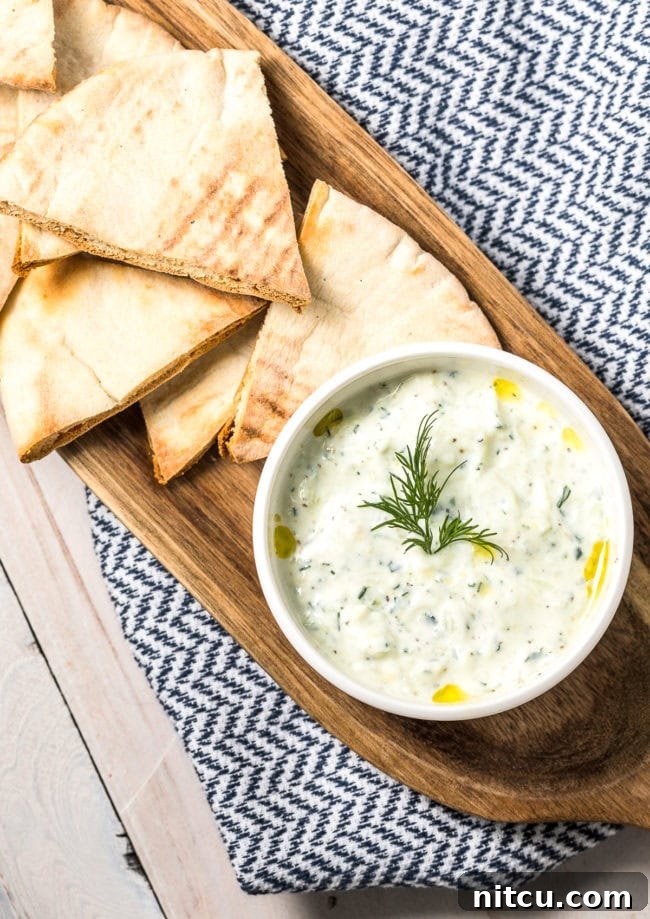 Refreshing Greek Cucumber Dip 5 Tzatziki dip in a white bowl, placed on a wood platter with pita bread.