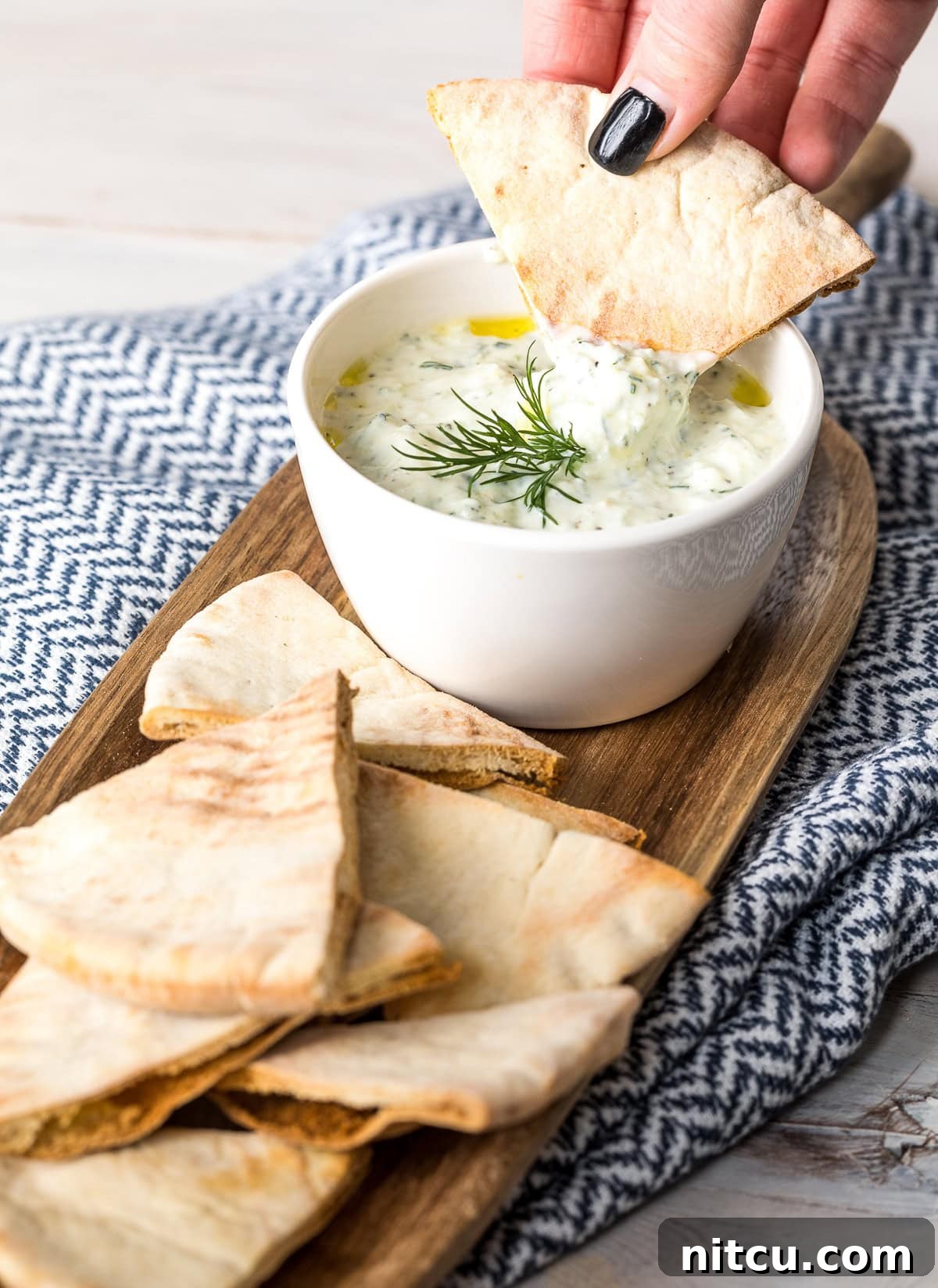 Refreshing Greek Cucumber Dip 9 A hand dipping a piece of pita bread in tzatziki sauce that's in a white bowl.