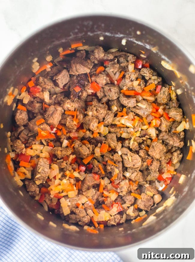 Brewmaster's Chili 4 Diced steak and vibrant vegetables sizzling in a large stock pot, preparing the flavorful base for the chili.