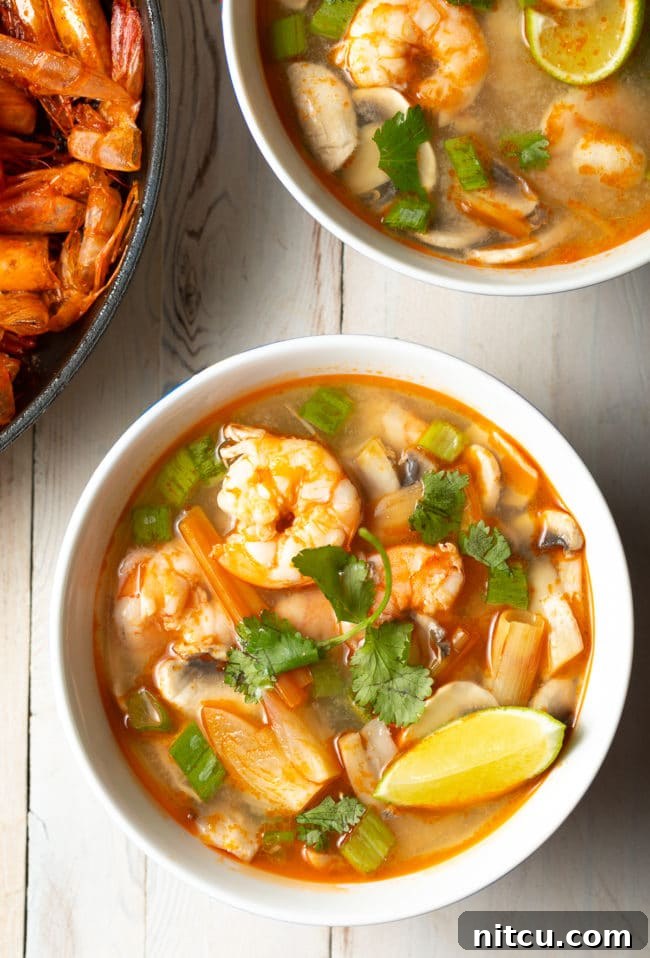 Spicy Thai Tom Yum Soup 2 Overhead shot of a vibrant bowl of Tom Yum soup, garnished with fresh cilantro and bright lime wedges, showcasing its rich colors and enticing aroma.