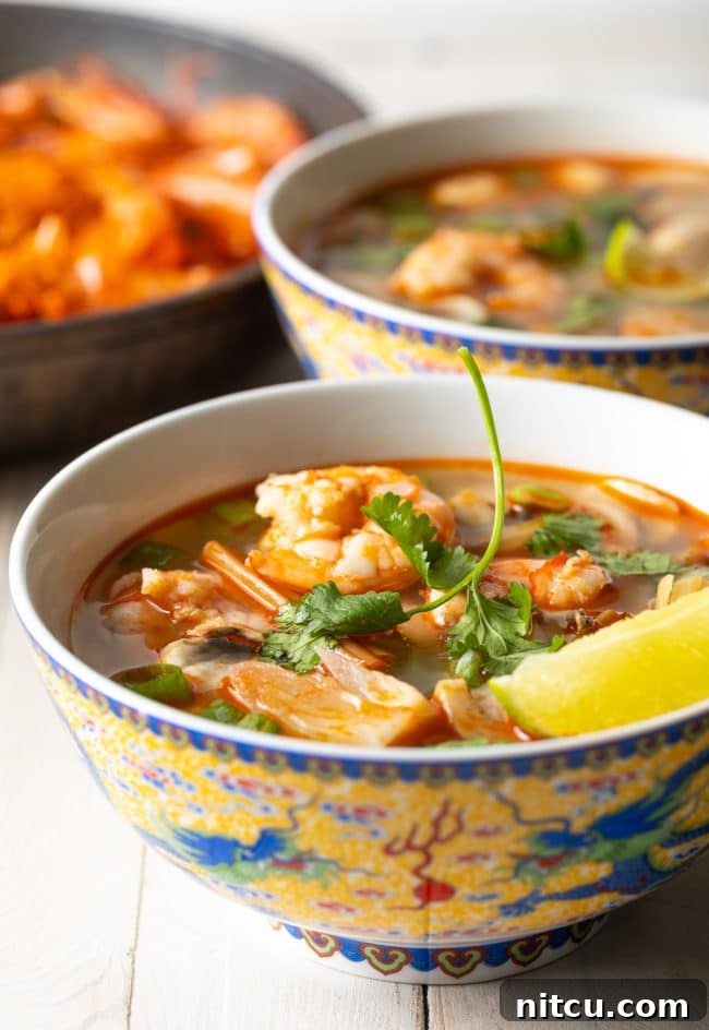 Spicy Thai Tom Yum Soup 4 Two steaming bowls of Thai Hot and Sour Soup, artfully garnished with fresh cilantro and a lime wedge, ready to be enjoyed.