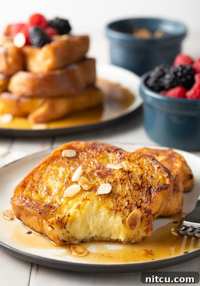 Golden Fluffy French Toast Perfection 11 Two slices of pain perdu with a bit taken out of it on a white plate.