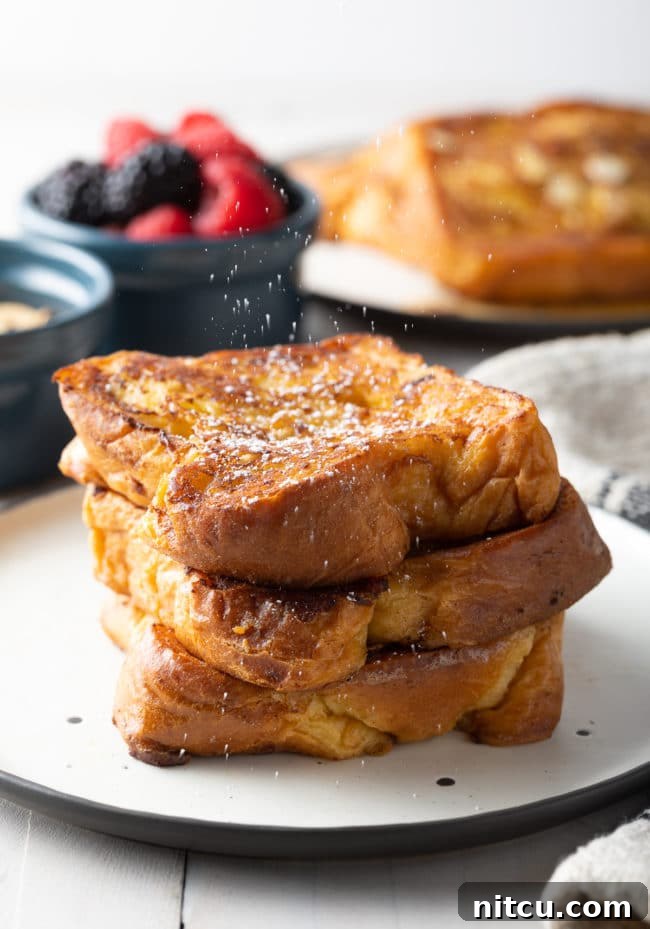 Golden Fluffy French Toast Perfection 3 A stack of french toast on a white plate with powdered sugar dusting the top.