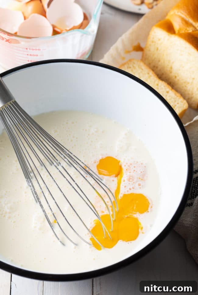 Golden Fluffy French Toast Perfection 5 Egg mixture in a white bowl with a whisk.
