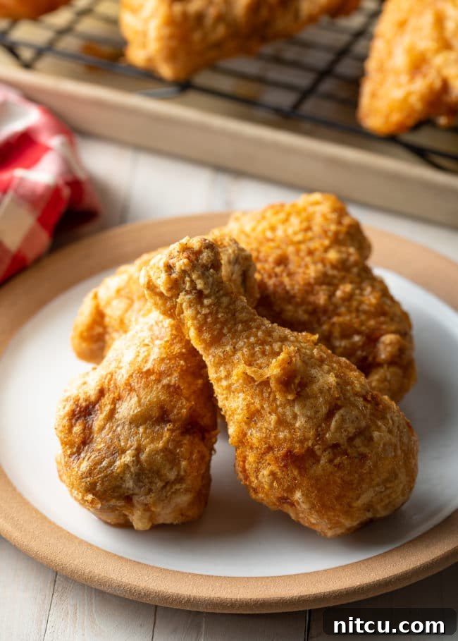 Ultimate Tavern Style Fried Chicken 2 Three pieces of golden-brown tavern fried chicken on a white plate, showcasing its light, crispy skin.