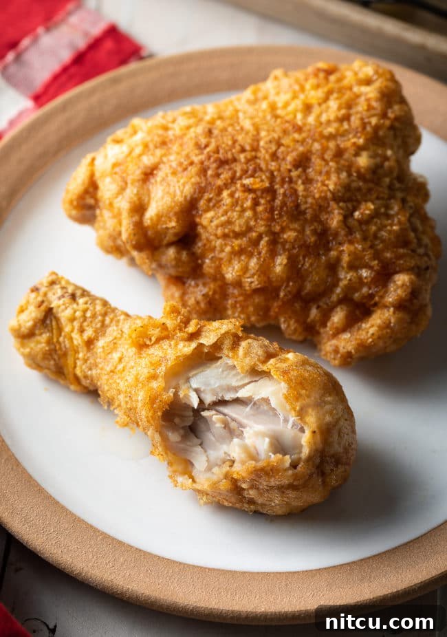 Ultimate Tavern Style Fried Chicken 11 Top-down view of a breaded fried chicken thigh and drumstick on a plate, with a bite taken from the drumstick.