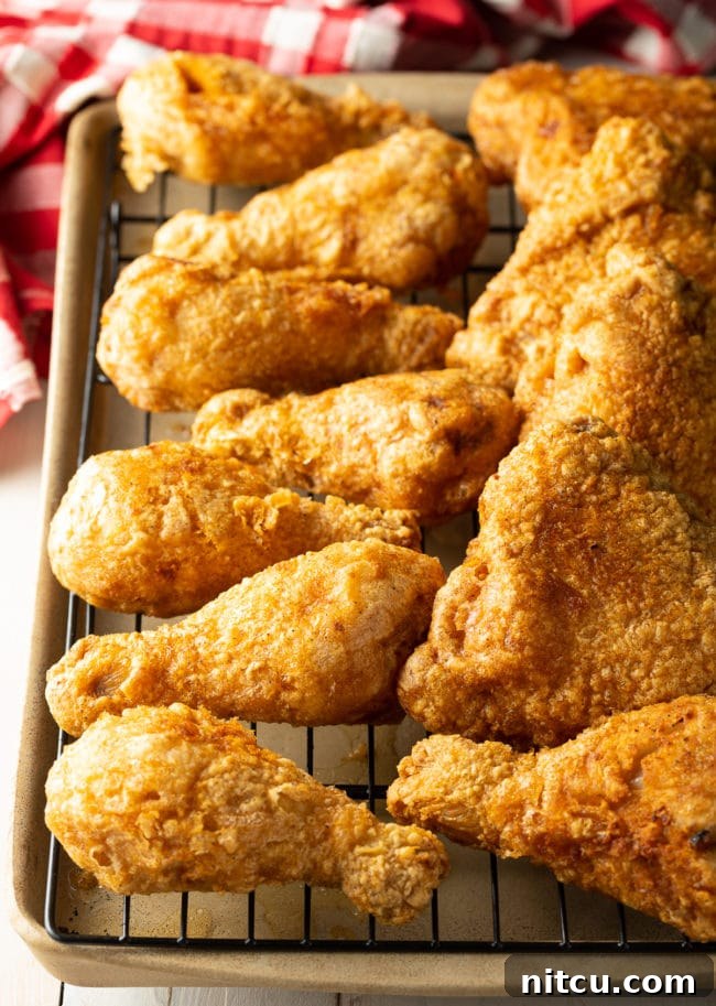 Ultimate Tavern Style Fried Chicken 3 Several pieces of golden-brown fried chicken legs and thighs resting on a wire rack over a baking sheet, allowing excess oil to drip.