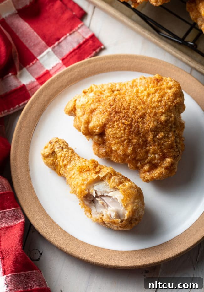 Ultimate Tavern Style Fried Chicken 4 A top-down view of a breaded fried chicken thigh and drumstick on a white plate, with a bite taken from the drumstick to show the juicy interior.