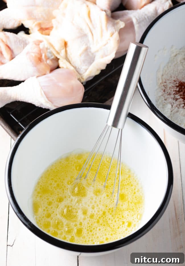 Ultimate Tavern Style Fried Chicken 5 Whisked egg whites in a white mixing bowl with a metal whisk, showing their frothy texture.