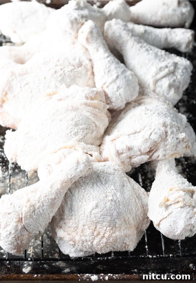 Ultimate Tavern Style Fried Chicken 6 Several pieces of skin-on and bone-in chicken, freshly dredged in flour, laid out on a wire rack to rest.