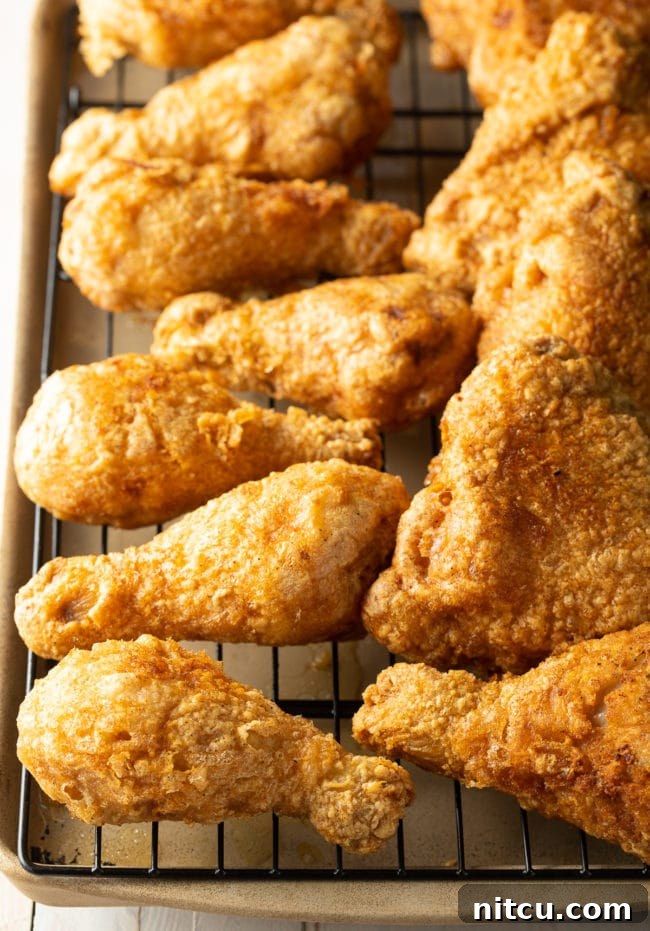 Ultimate Tavern Style Fried Chicken 8 Several pieces of perfectly fried chicken legs and thighs arranged on a wire rack over a baking sheet, glistening golden-brown.
