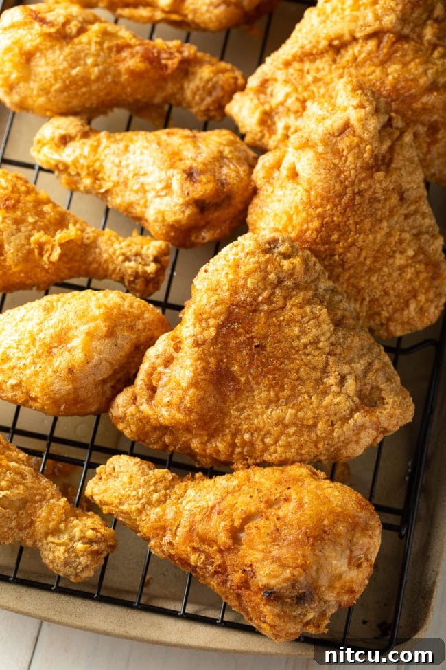 Ultimate Tavern Style Fried Chicken 9 Several pieces of golden-brown fried chicken legs and thighs neatly arranged on a wire rack over a baking sheet.